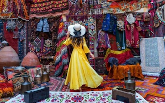 Woman in yellow dress exploring a vibrant Moroccan market with colorful textiles in Marrakech.
