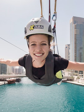 Person ziplining over Dubai Marina with skyscrapers in the background.