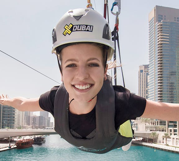 Person ziplining over Dubai Marina with skyscrapers in the background.