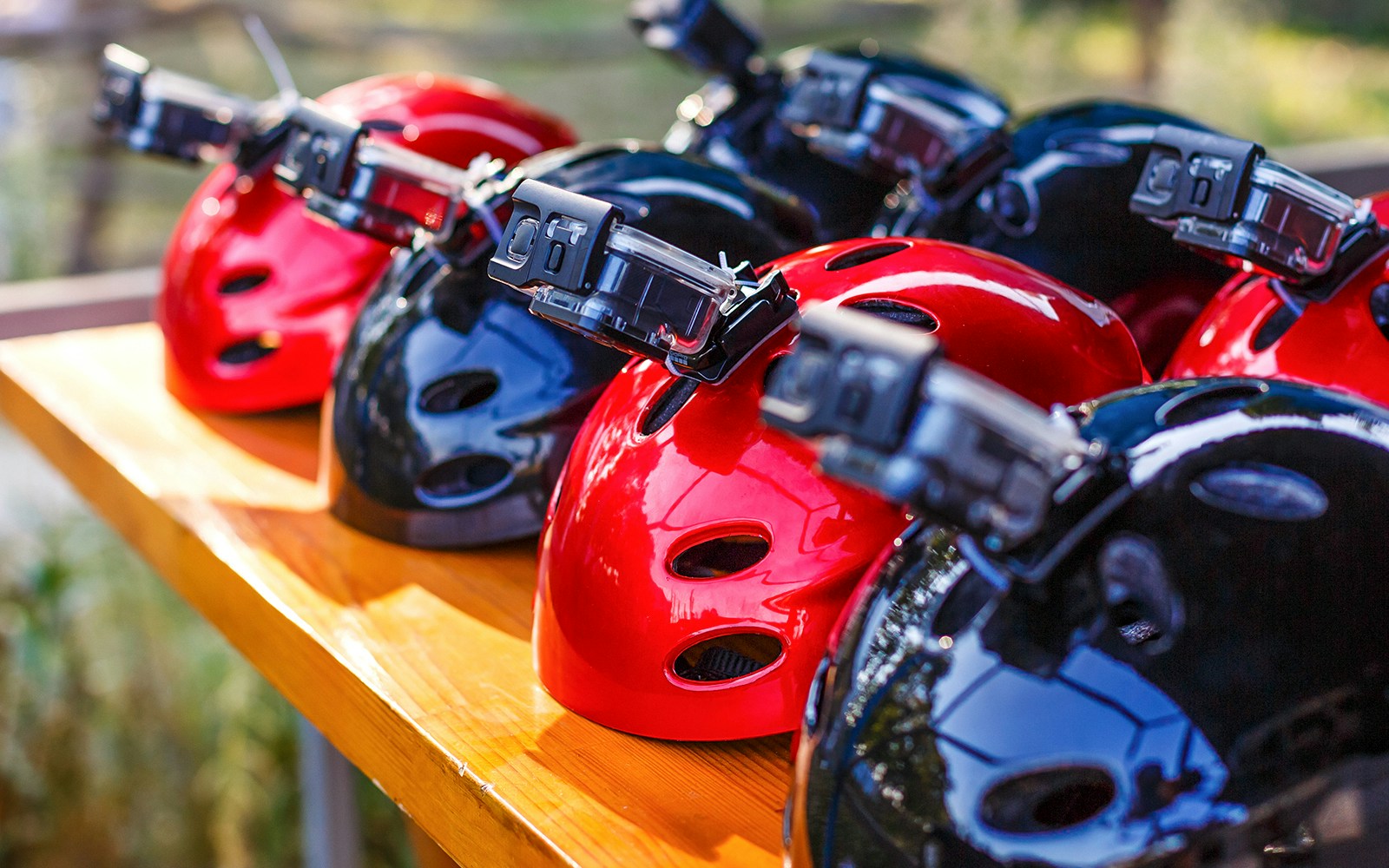 Helmets with mounted cameras on a wooden table.