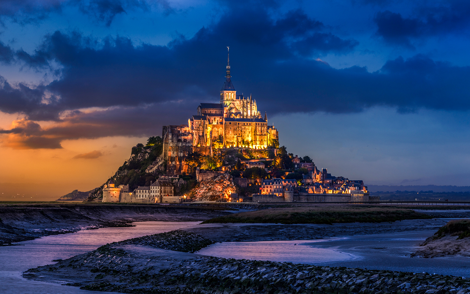 Mont Saint Michel illuminated at night with a dramatic sky in Normandy, France.