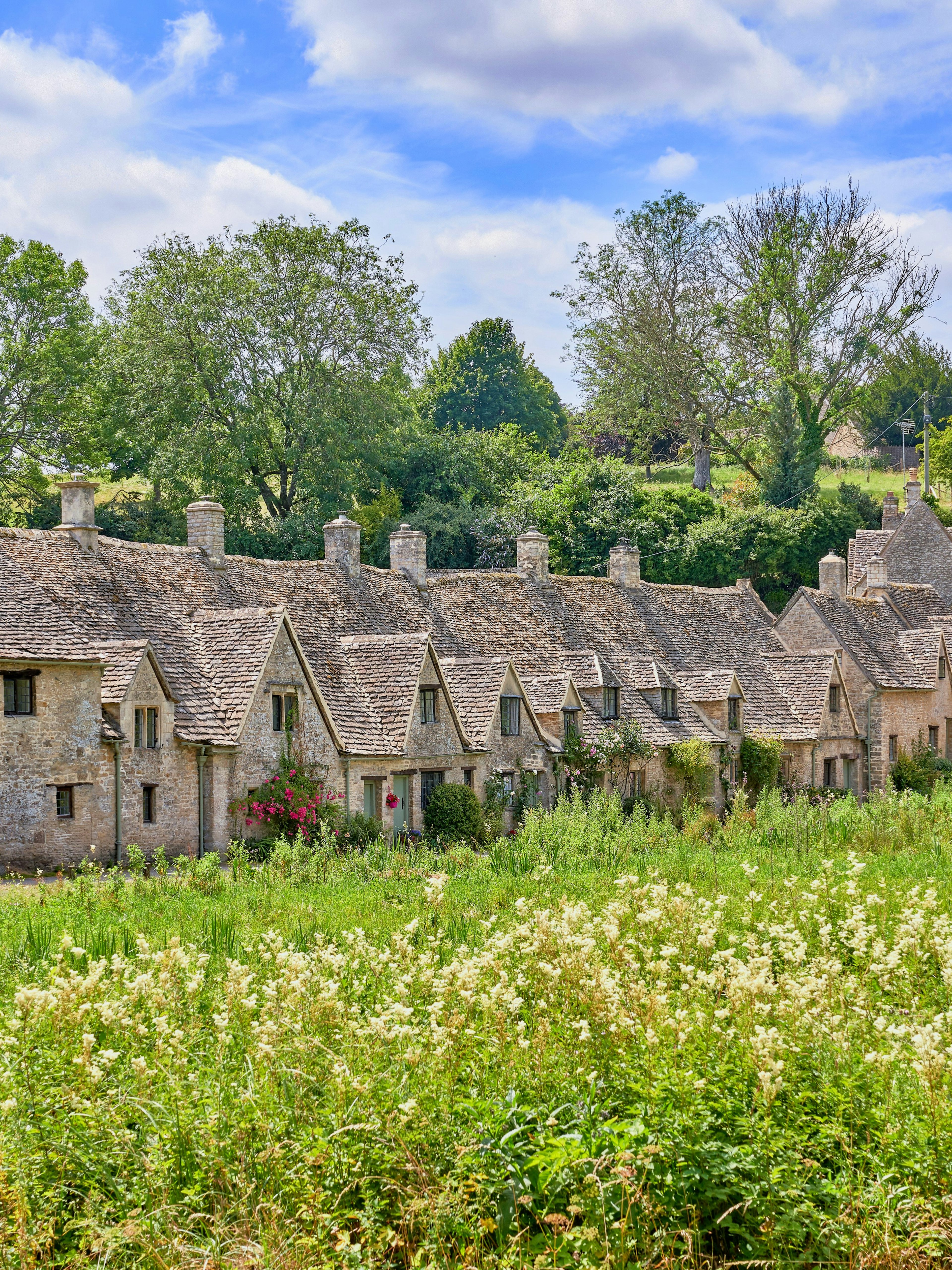 Arlington Row cottages in Bibury, Cotswolds, surrounded by lush greenery in summer.