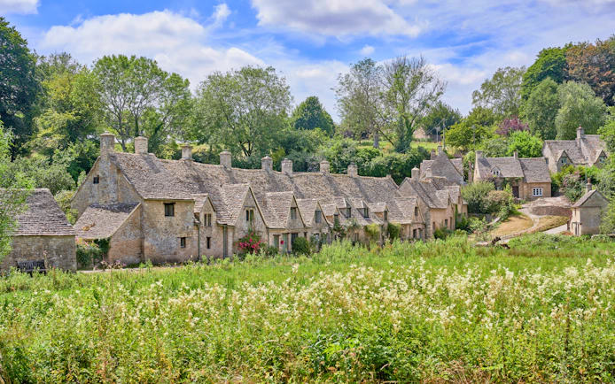 Arlington Row cottages in Bibury, Cotswolds, surrounded by lush greenery in summer.