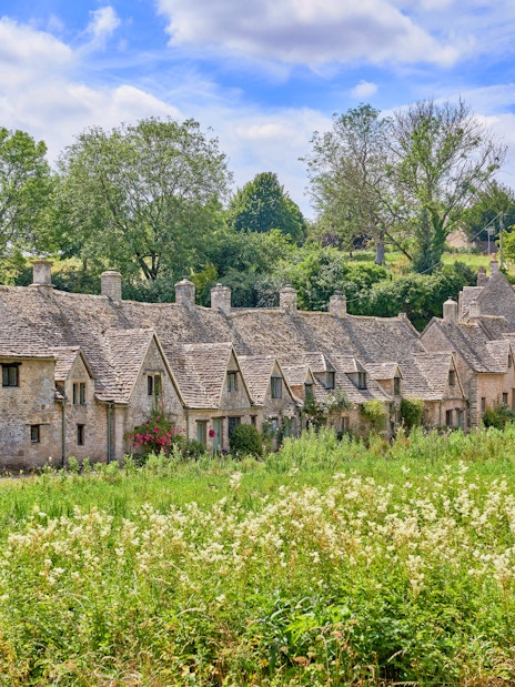 Arlington Row cottages in Bibury, Cotswolds, surrounded by lush greenery in summer.