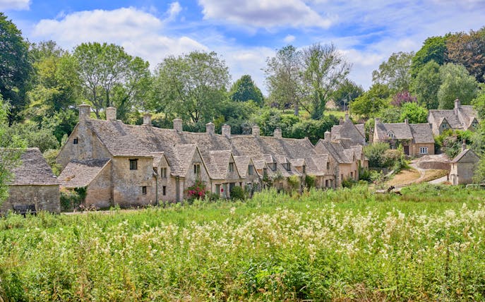 Arlington Row cottages in Bibury, Cotswolds, surrounded by lush greenery in summer.