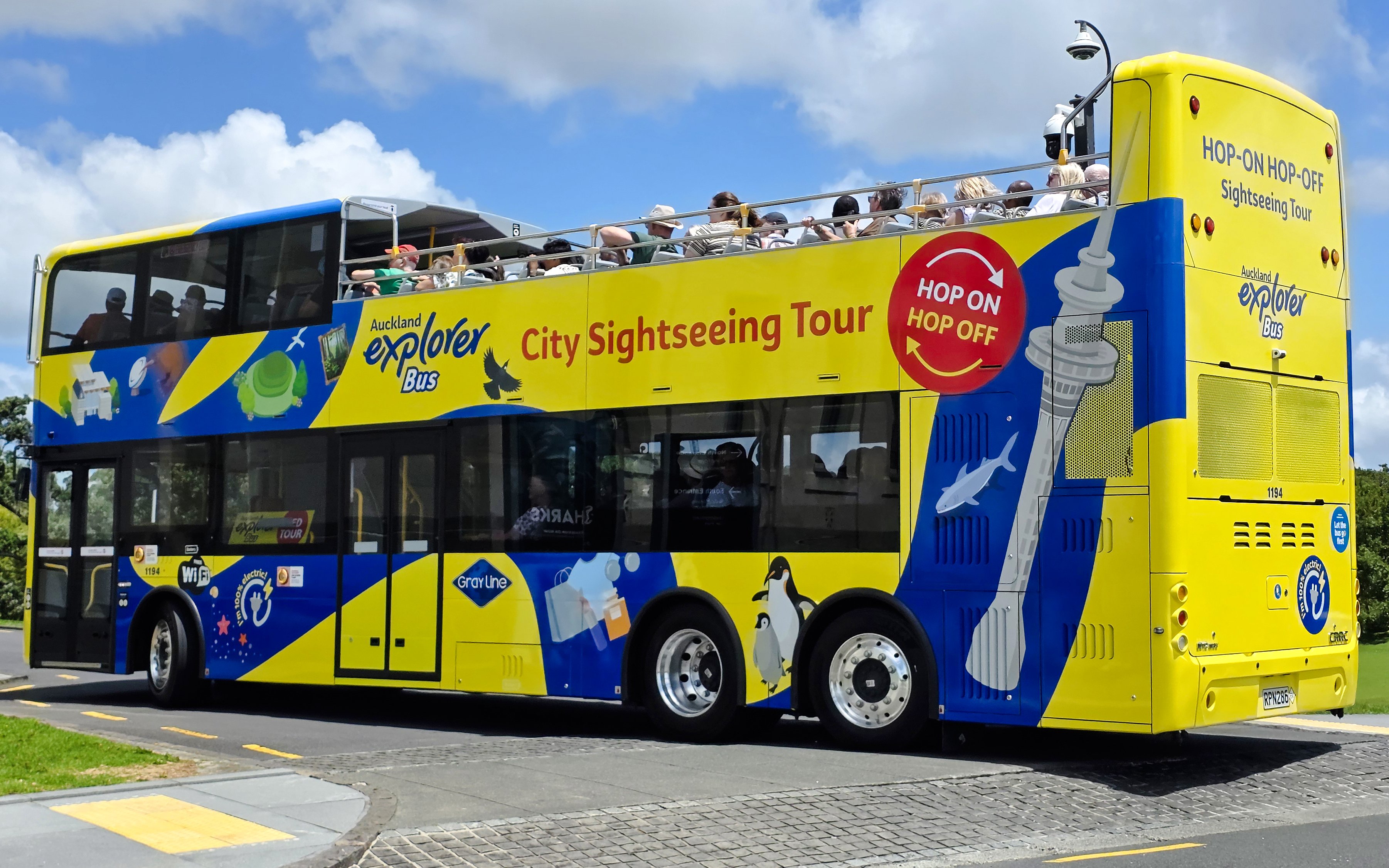 Auckland Explorer Bus on a sunny day with tourists on the upper deck.