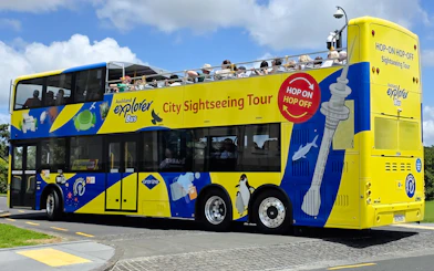 Auckland Explorer Bus on a sunny day with tourists on the upper deck.