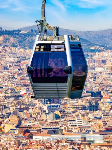 Montjuic Cable Car over Barcelona cityscape with distant hills.
