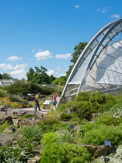 Kew Gardens glasshouse with visitors walking through lush gardens.
