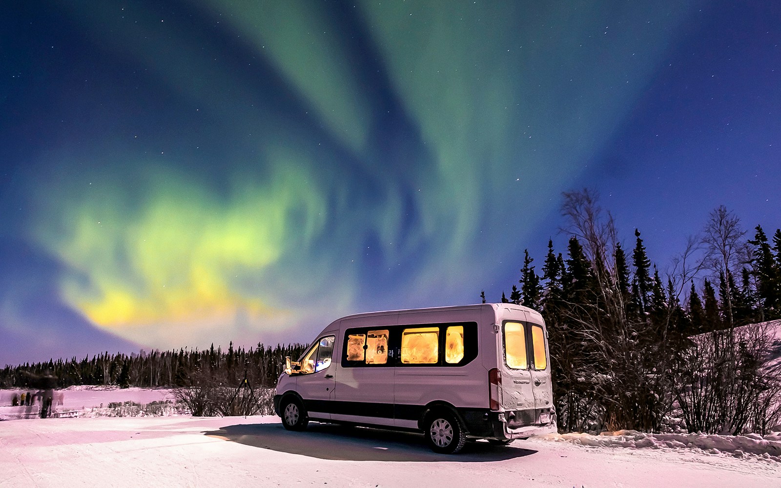 Minibus under Northern Lights in snowy landscape.