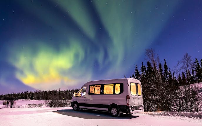 Minibus under Northern Lights in snowy landscape.