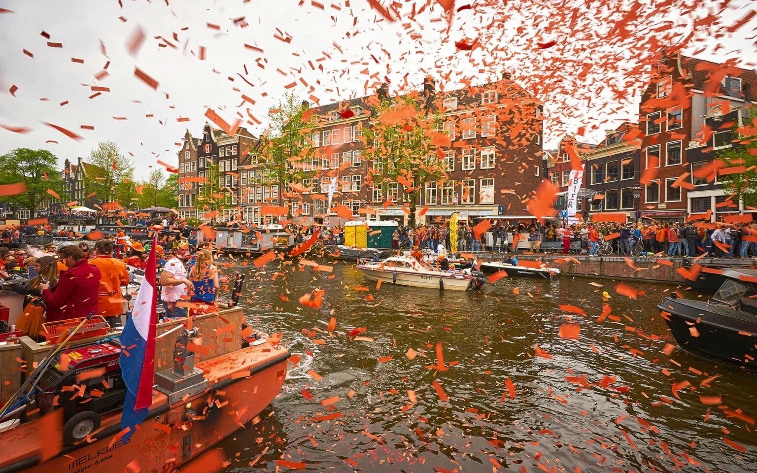 Amsterdam Kingsday cruise with orange confetti on canal, boats, and historic buildings.