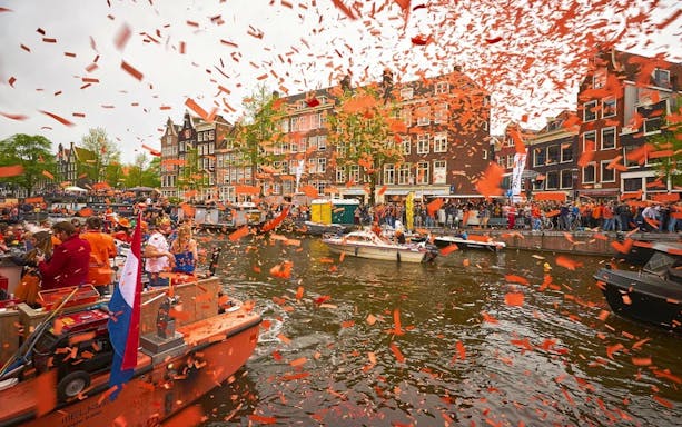 Amsterdam Kingsday cruise with orange confetti on canal, boats, and historic buildings.