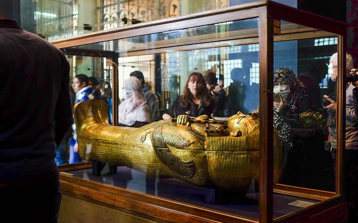 Golden sarcophagus displayed in a museum exhibit with visitors observing.