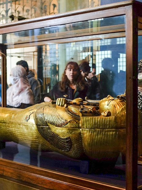 Golden sarcophagus displayed in a museum exhibit with visitors observing.