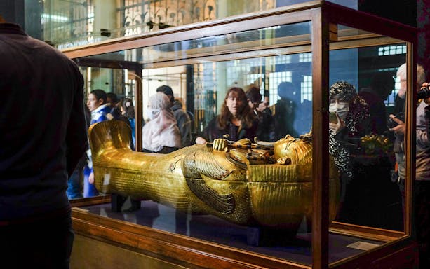 Golden sarcophagus displayed in a museum exhibit with visitors observing.