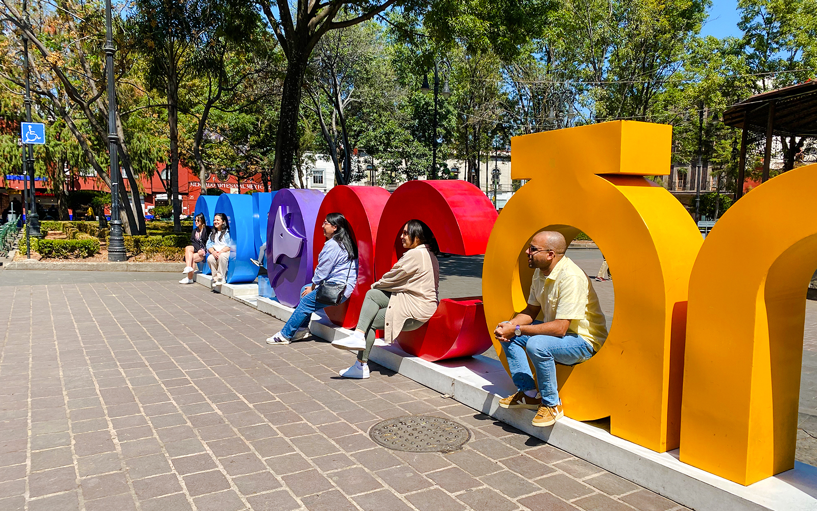 People sitting on colorful Coyoacán sign in a park setting.