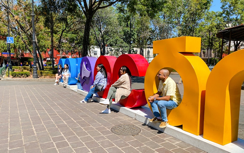 People sitting on colorful Coyoacán sign in a park setting.