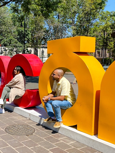 People sitting on colorful Coyoacán sign in a park setting.