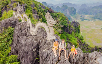 Tourists sitting near dragon statue on limestone mountain at Hang Mua viewpoint, Vietnam.