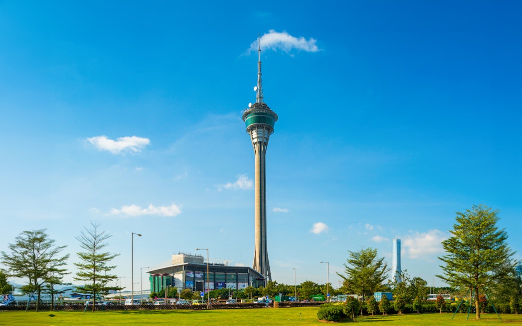 Macau Tower against a clear blue sky with surrounding greenery.