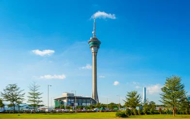 Macau Tower against a clear blue sky with surrounding greenery.