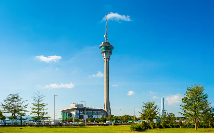 Macau Tower against a clear blue sky with surrounding greenery.