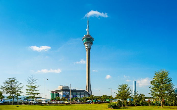 Macau Tower against a clear blue sky with surrounding greenery.