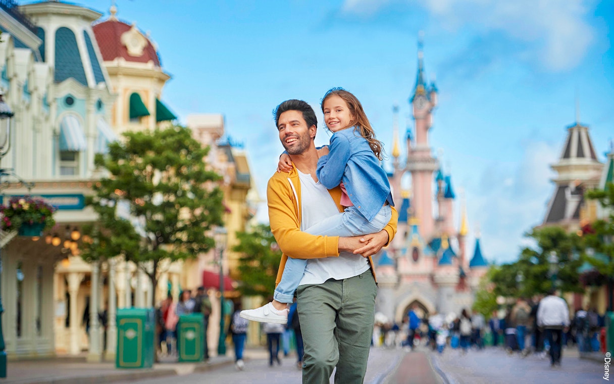 Father and daughter smiling in front of Sleeping Beauty Castle at Disneyland Paris.