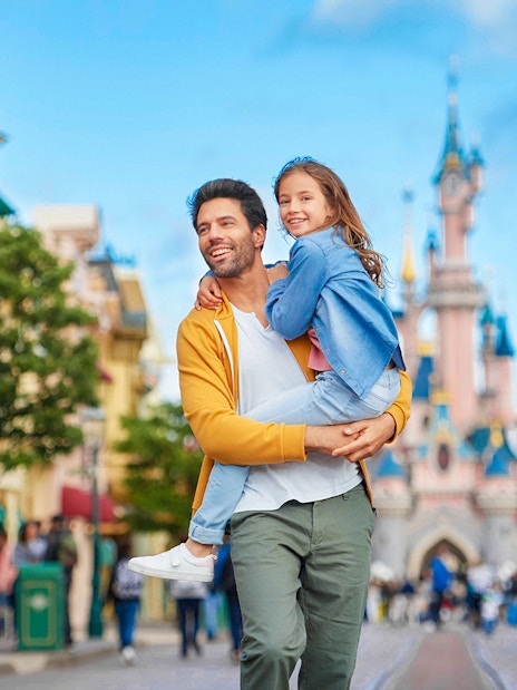 Father and daughter smiling in front of Sleeping Beauty Castle at Disneyland Paris.