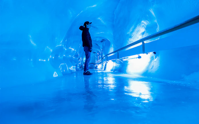 Person exploring Mount Titlis Glacier Cave with icy blue walls.