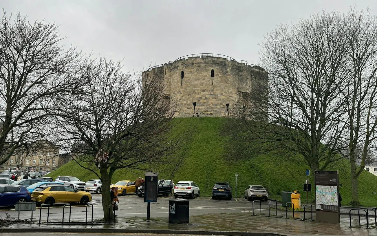 Clifford's Tower in York, surrounded by trees and parked cars, part of the Ghosts of York tour.