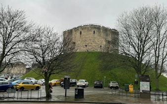 Clifford's Tower in York, surrounded by trees and parked cars, part of the Ghosts of York tour.