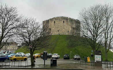 Clifford's Tower in York, surrounded by trees and parked cars, part of the Ghosts of York tour.