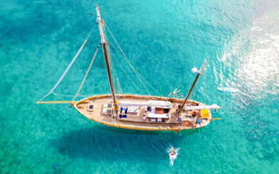 Sailing boat in clear waters near Frioul Archipelago, France, with people swimming nearby.