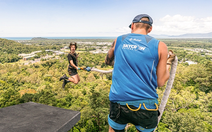 Bungy jumper mid-air with instructor overlooking Cairns landscape.