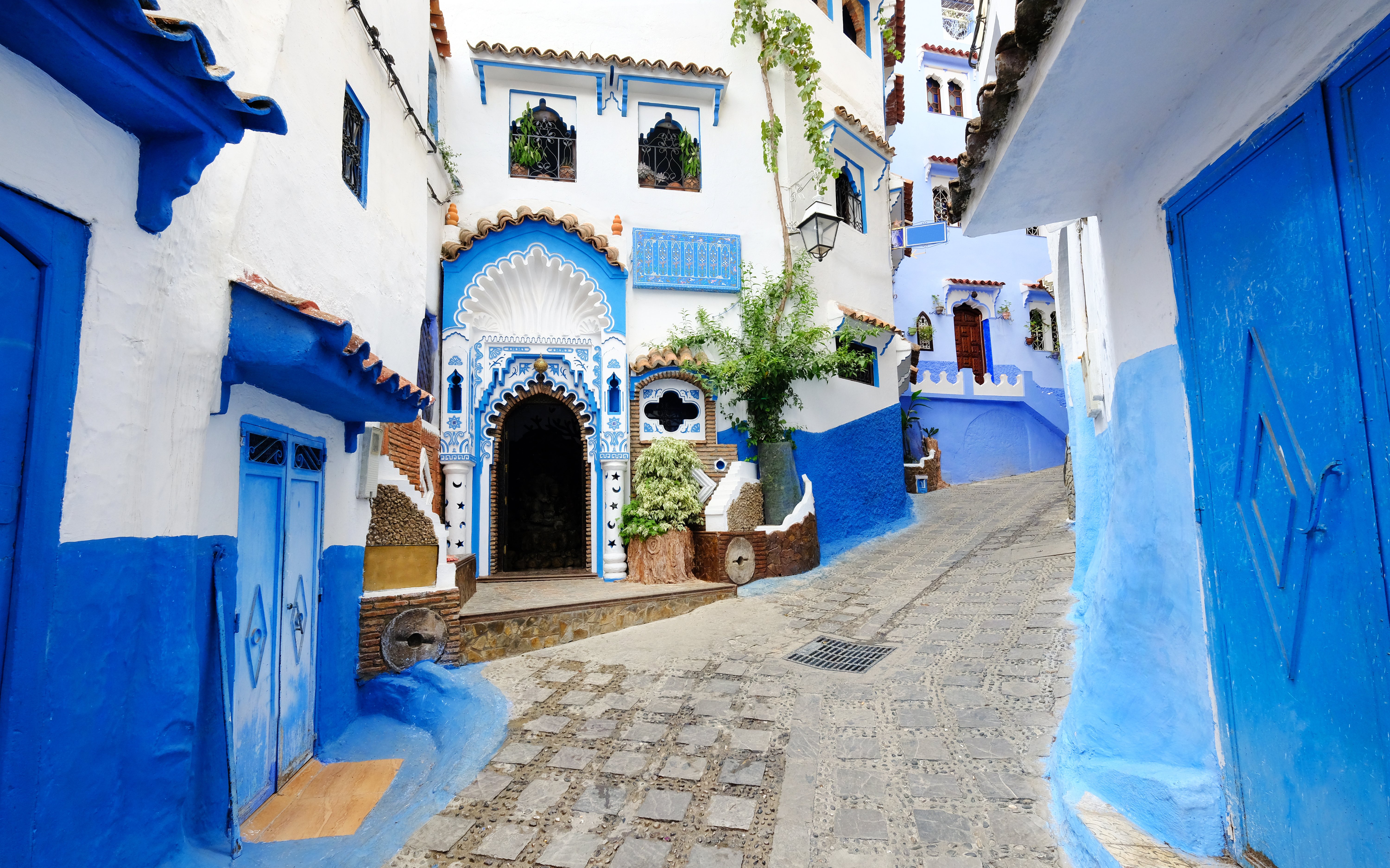 Blue-walled street in Chefchaouen, Morocco with ornate doorways and cobblestone path.