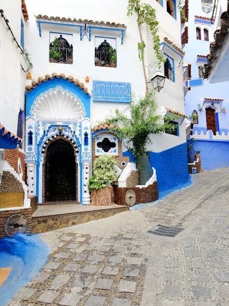 Blue-walled street in Chefchaouen, Morocco with ornate doorways and cobblestone path.
