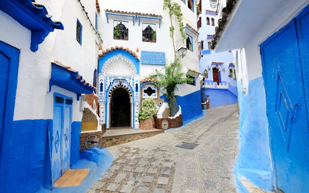 Blue-walled street in Chefchaouen, Morocco with ornate doorways and cobblestone path.