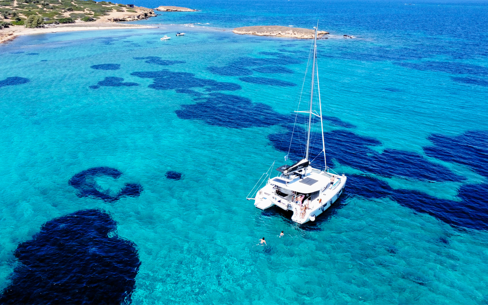 Catamaran sailing in clear turquoise waters near a rocky coastline.