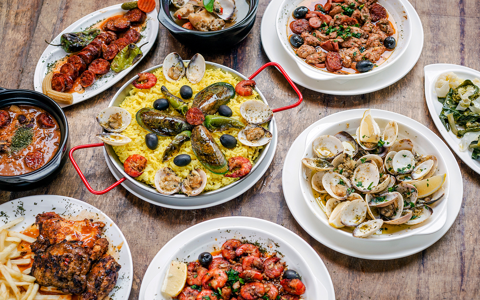 Portuguese rustic tapas with clams, chorizo, and yellow rice on a wooden table.
