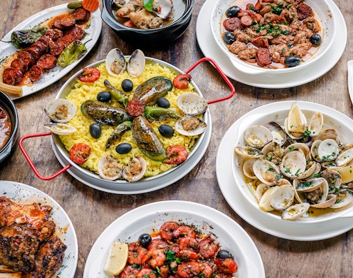 Portuguese rustic tapas with clams, chorizo, and yellow rice on a wooden table.