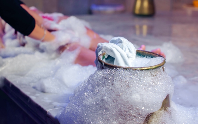 Foam massage in Turkish bath with bubbles and cloth on marble surface.