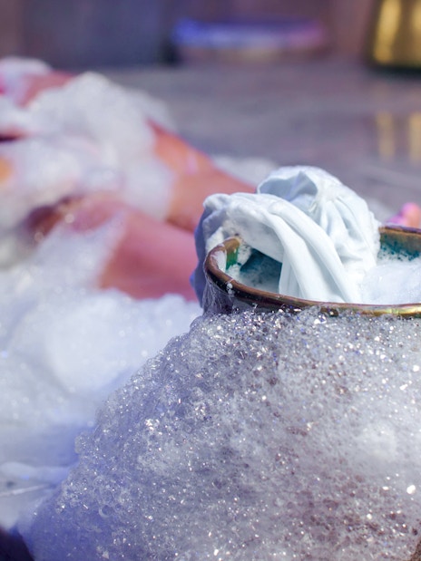 Foam massage in Turkish bath with bubbles and cloth on marble surface.