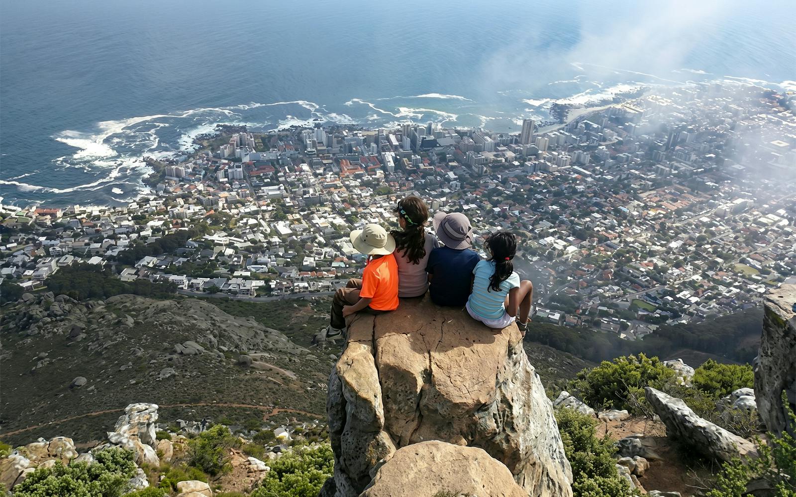 Hikers sitting on Lion's Head summit overlooking Cape Town cityscape and ocean.