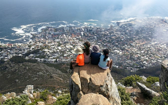 Hikers sitting on Lion's Head summit overlooking Cape Town cityscape and ocean.