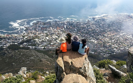 Hikers sitting on Lion's Head summit overlooking Cape Town cityscape and ocean.