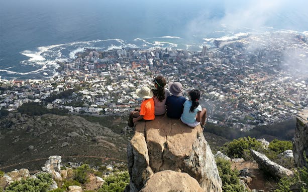 Hikers sitting on Lion's Head summit overlooking Cape Town cityscape and ocean.