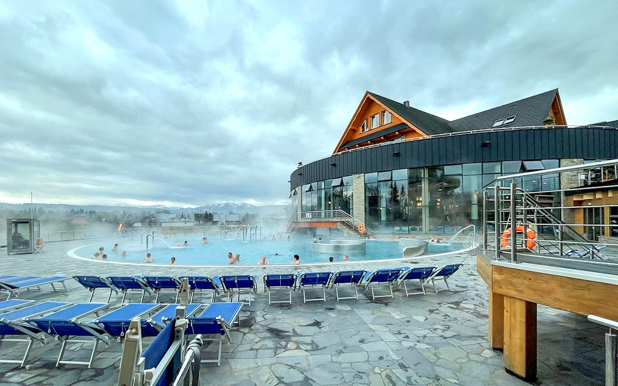 Outdoor pool at Zakopane Thermal Baths with people relaxing, surrounded by mountains.