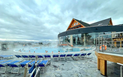Outdoor pool at Zakopane Thermal Baths with people relaxing, surrounded by mountains.